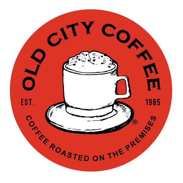 Red circular Old City Coffee logo showing the vintage hand-drawn white coffee mug with frothy coffee on a saucer in the center. Text around the perimeter reads "Old City Coffee Est. 1985 Coffee Roasted on the Premises"