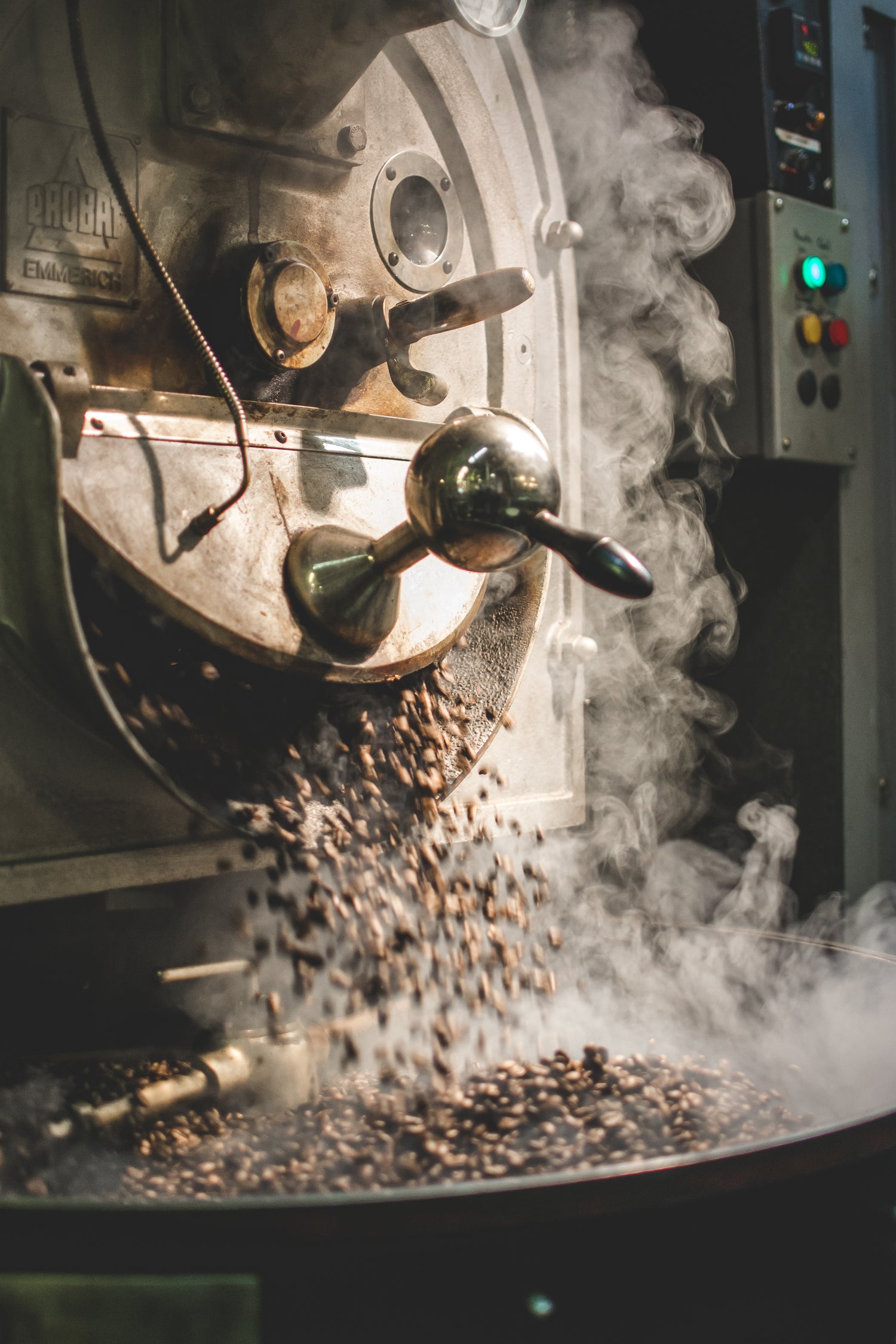 Vintage coffee roaster dropping freshly roasted coffee beans into the cooling tray, with steam billowing around the roaster