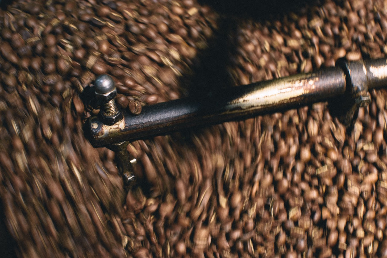 Coffee beans being quickly stirred and cooled in the cooling tray of a vintage roaster. Aerial view of the drum and mixing arm